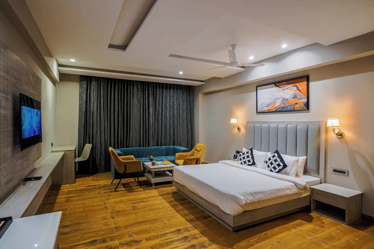 A modern hotel room with a bed, a sofa, a TV, a ceiling fan, and a painting on the wall.