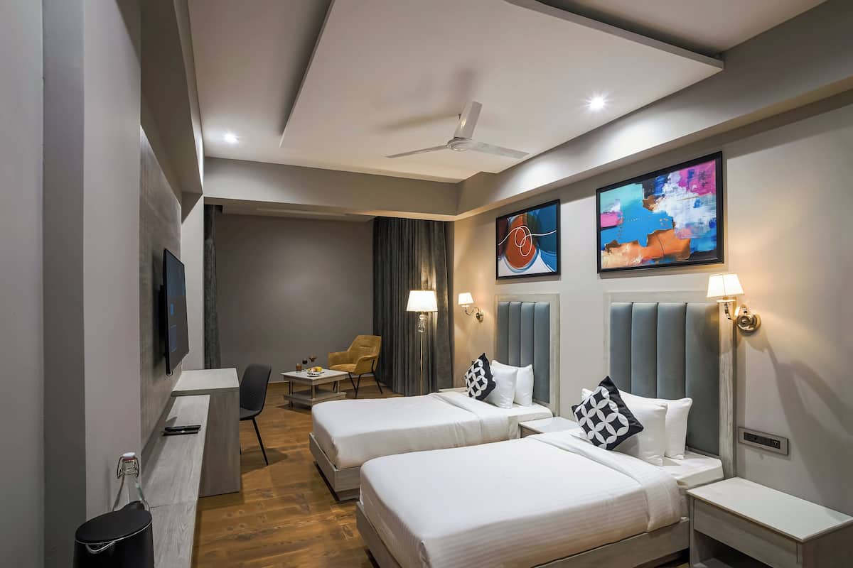 A hotel room with two beds, a desk, a chair, a TV, and artwork on the walls.