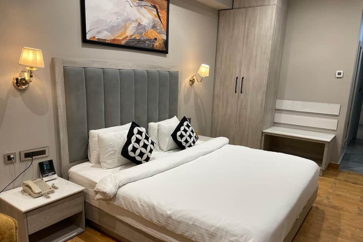 A modern bedroom with a large bed, two bedside tables with lamps, a nightstand with a phone, and a wardrobe.