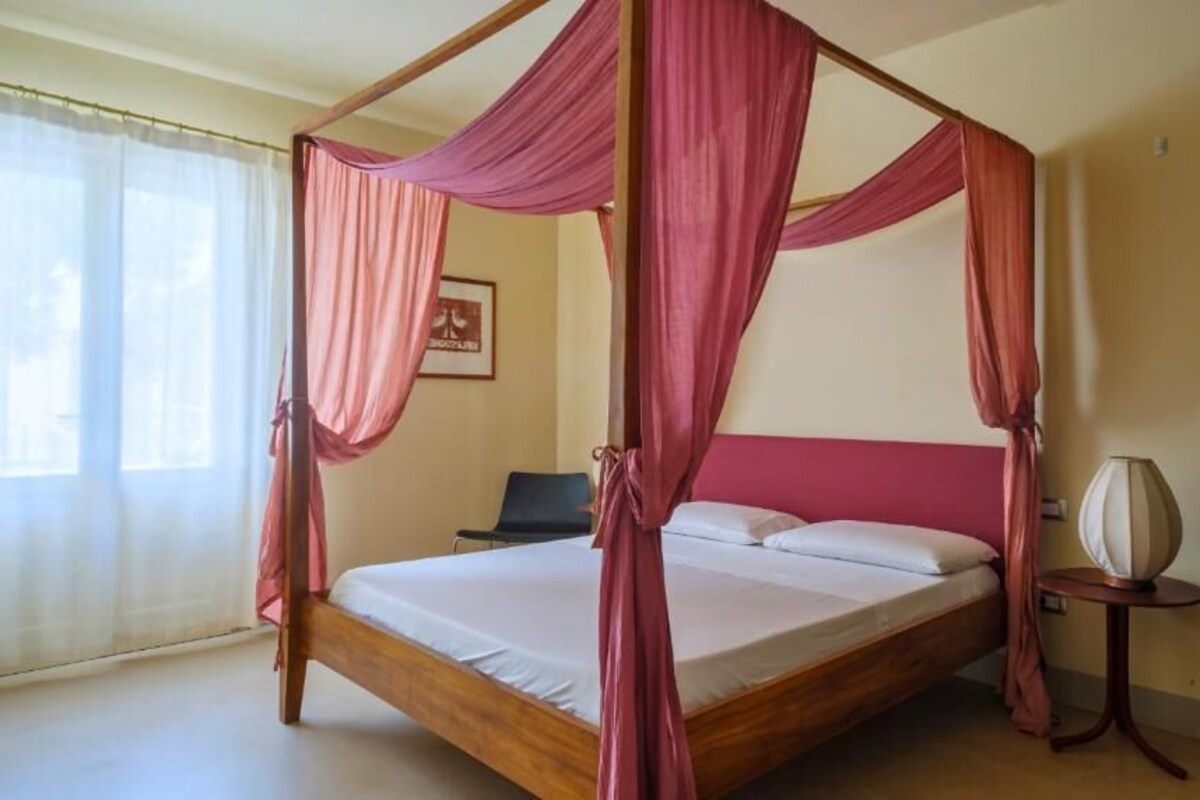 A four-poster bed with pink drapes, a bedside table with a lamp, and a framed picture on the wall.