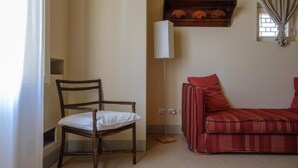 A room with a wooden chair, a red sofa, a floor lamp, and a shelf with decorative items. - Masseria Bernardini (Nardò)