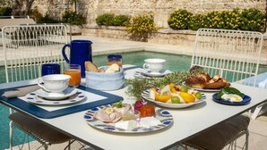 A dining table with breakfast items and a view of a pool and stone wall. - Masseria Bernardini (Nardò)