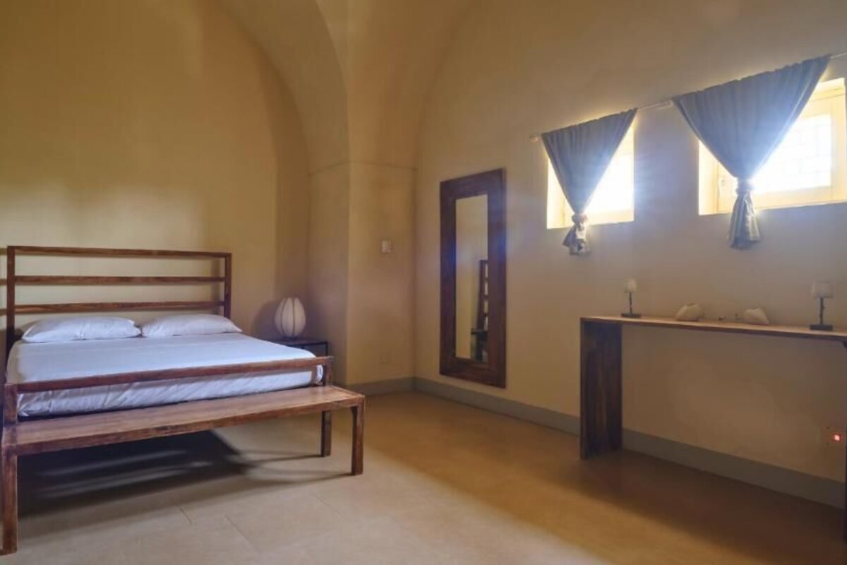 A bedroom with a wooden bed, a bedside table, a mirror, and a console table with lamps.