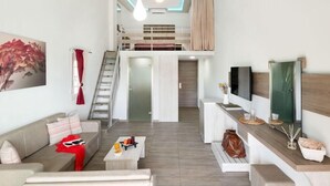 Un salon moderne avec un canapé, une table basse et un téléviseur. Un escalier mène à un niveau supérieur.