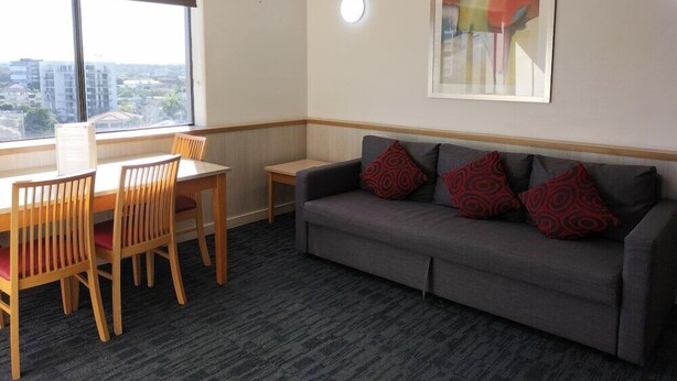 Una habitación con un sofá gris, una mesa de comedor con sillas y un amplio ventanal con vistas a la ciudad.