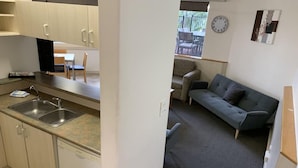 Un espacio habitable compacto con kitchenette, un sofá gris y un área de comedor visible a través de una puerta abierta.