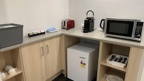Una kitchenette compacta con microondas, hervidor y refrigerador pequeño.