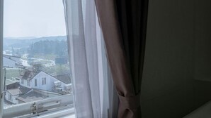 A window with a view of a residential area, curtains partially drawn, and a glimpse of a building with a flat roof and satellite dishes. - Ken Apos S House Backpackers Downtown (Da Lat)