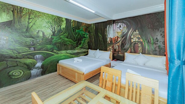 A room with two beds, a wooden chair, a small table, and a mural of a forest scene. - Ken Apos S House Backpackers Downtown (Da Lat)