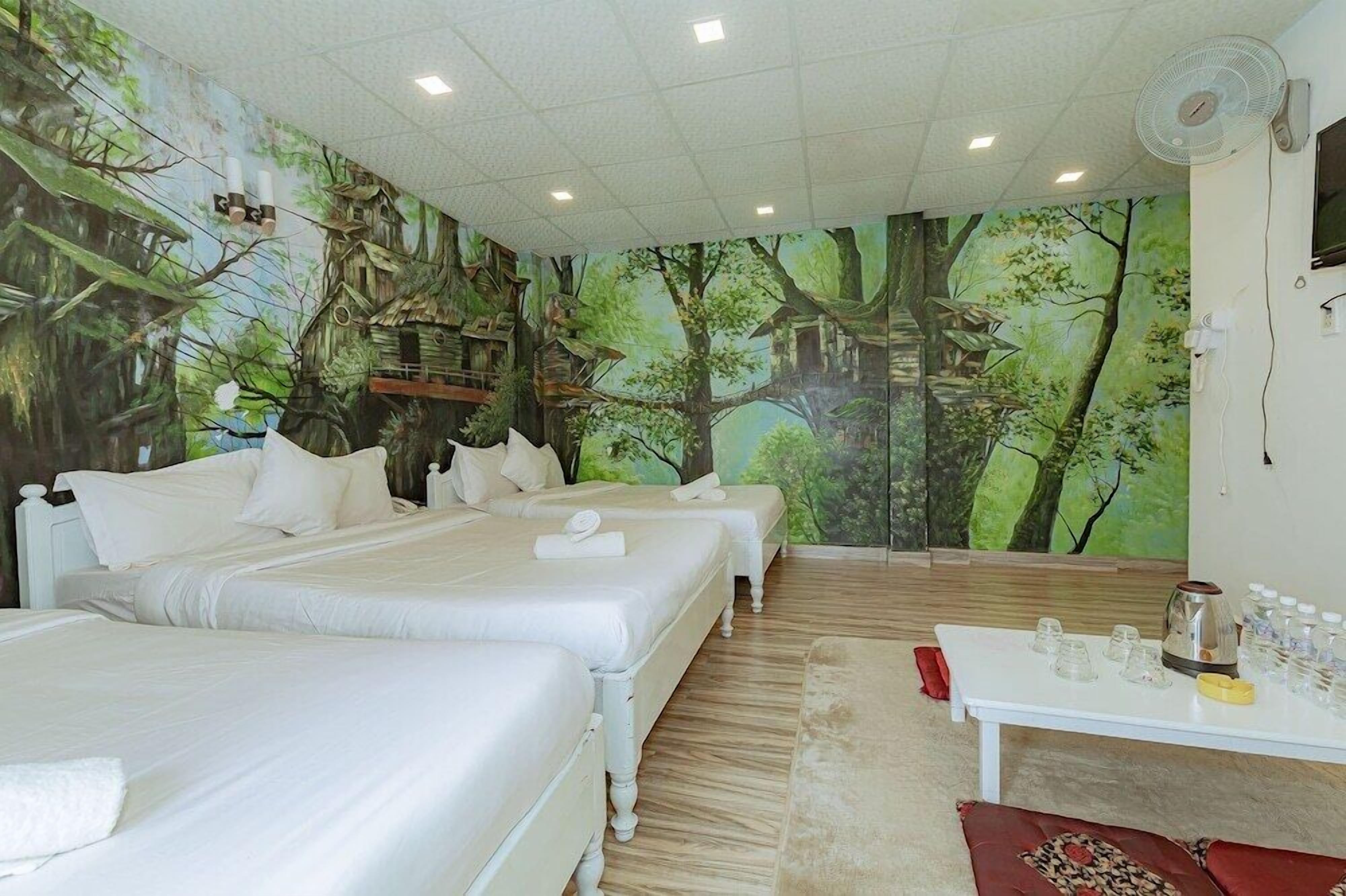 A room with two beds, a white table with glasses and a kettle, and a mural of a forest scene.