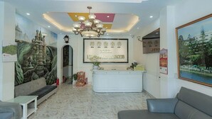 A hotel reception area with a marble floor, a reception desk, a chandelier, and a large mural on the wall. - Ken Apos S House Backpackers Downtown (Da Lat)