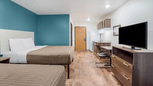 A hotel room with a bed, a desk, a TV, and a kitchenette.