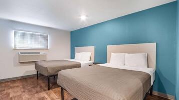 Habitación de hotel con dos camas, una ventana con persianas, unidad de aire acondicionado y suelo de madera.