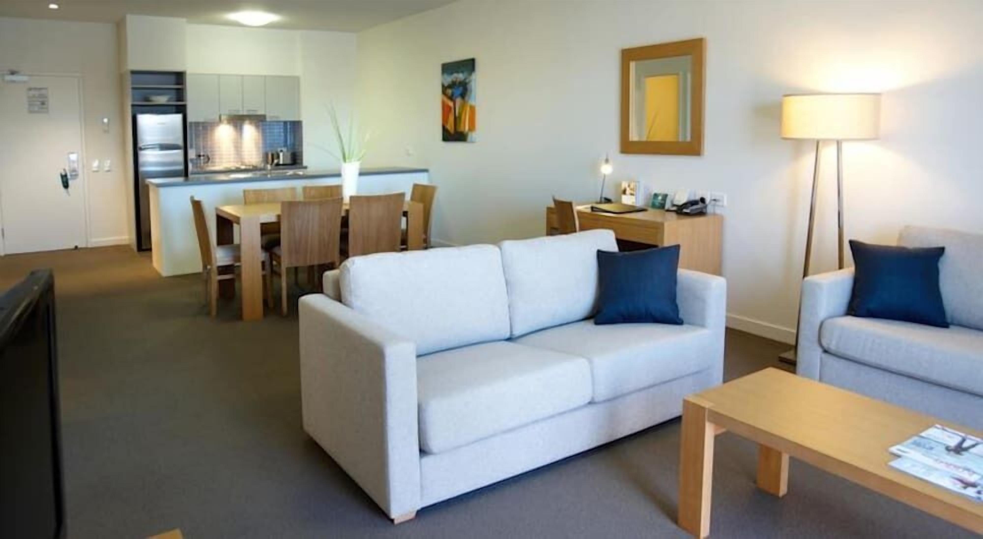Una sala de estar moderna con un sofá, un sillón más pequeño, una mesa de centro de madera y un comedor con una mesa y sillas.