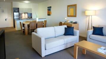 A modern living room with a sofa, a smaller armchair, a wooden coffee table, and a dining area with a table and chairs.