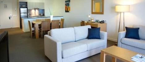 Una sala de estar moderna con un sofá, un sillón más pequeño, una mesa de centro de madera y un comedor con una mesa y sillas.