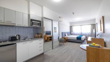 Une chambre d’hôtel moderne dotée d’une kitchenette, d’un lit aux accents bleus, d’un bureau et d’un coin repas.