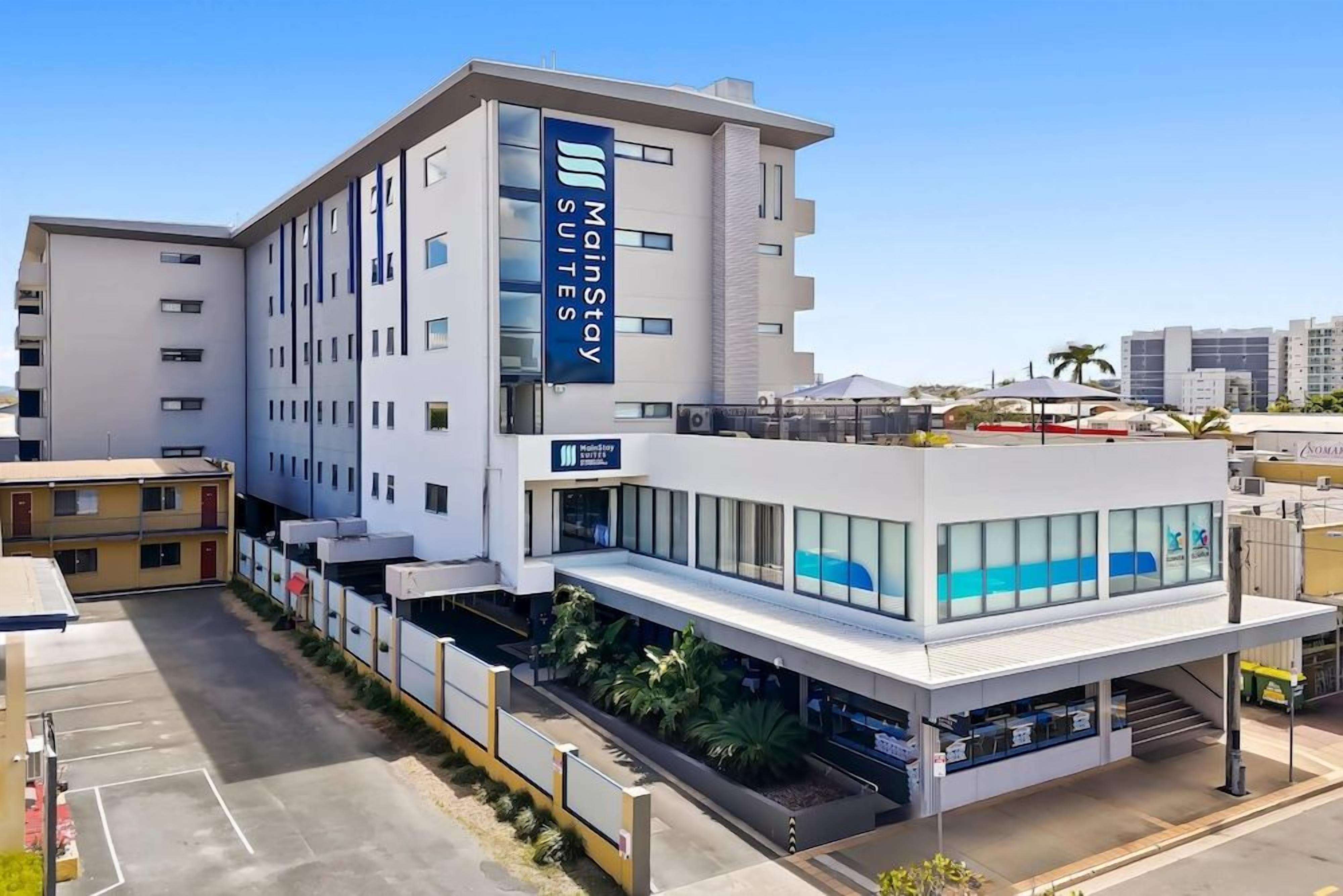A hotel with a modern design, featuring a prominent 'MainStay Suites' sign, a covered outdoor area, and a parking lot.