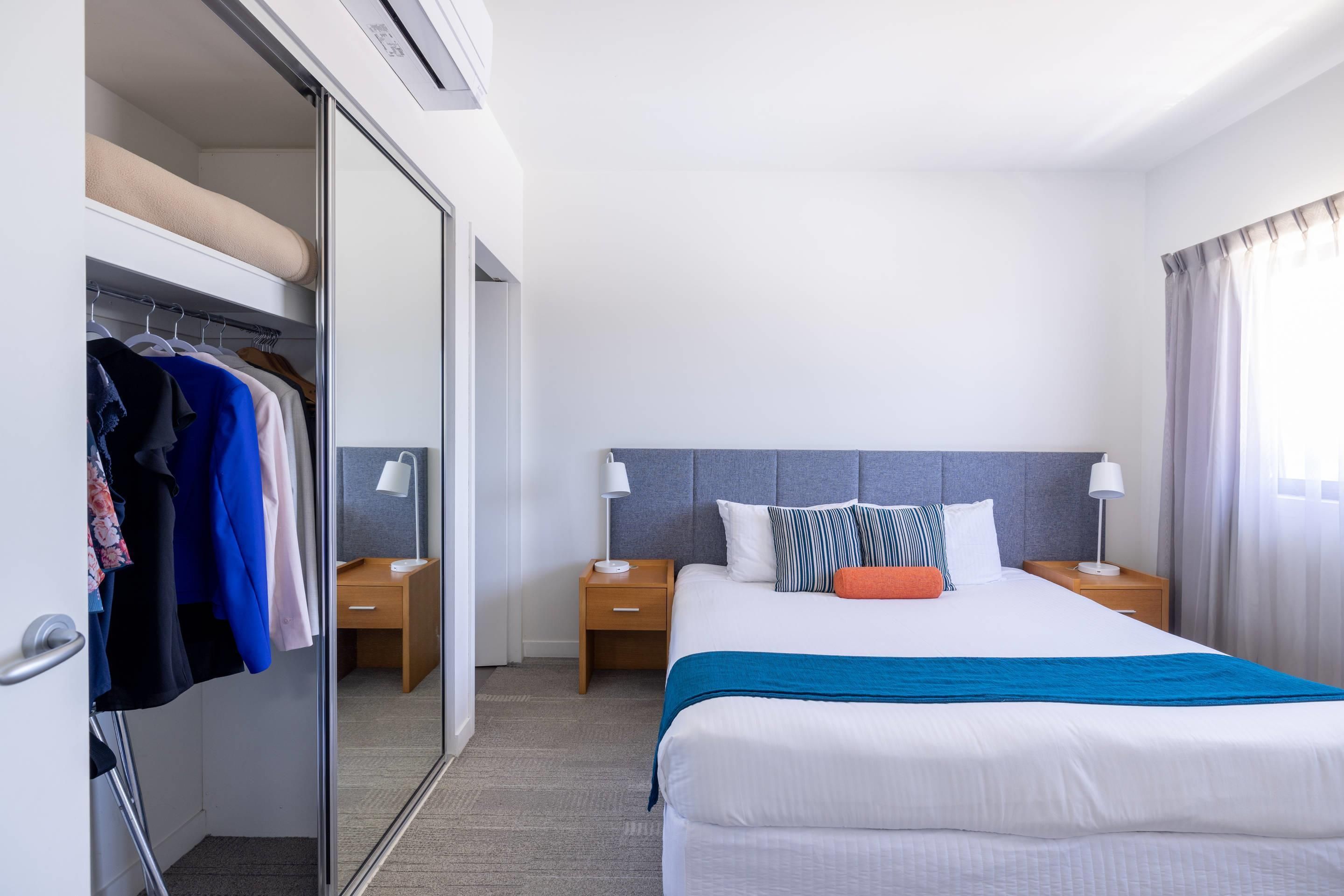 A hotel room with a bed, bedside tables, a wardrobe, and a mirror.
