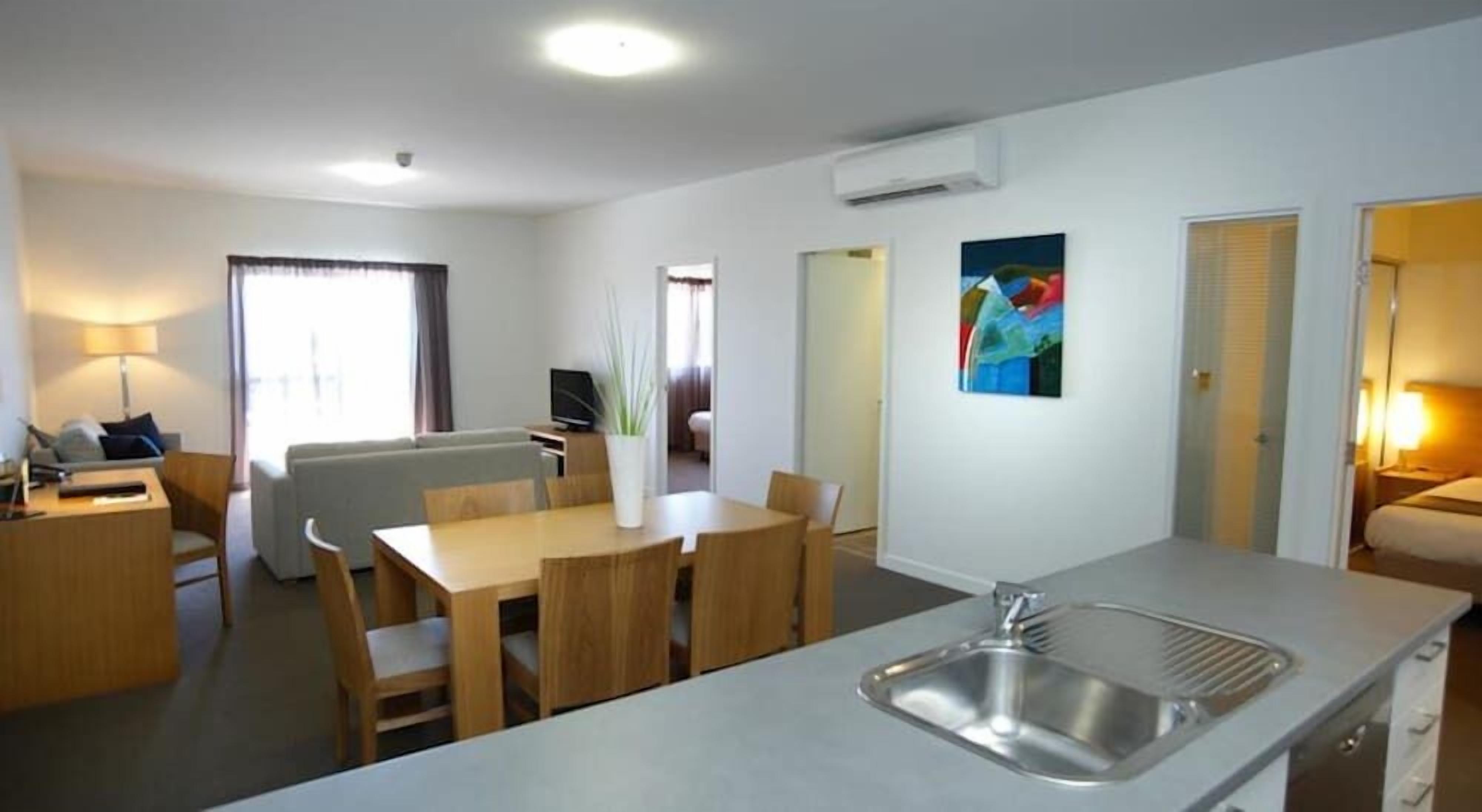 A modern kitchen with a central island, a dining area with wooden furniture, and a living space with a sofa and a TV.