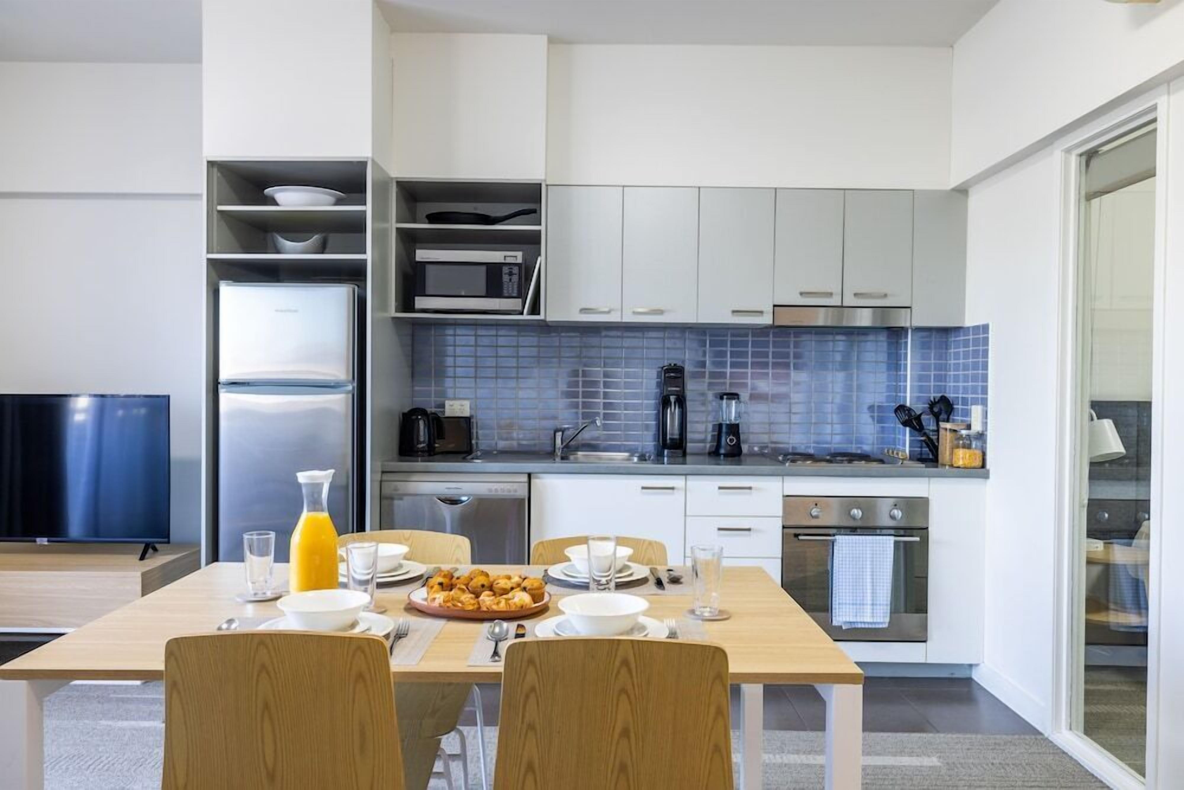 A modern kitchen with white cabinets, a blue tiled backsplash, and stainless steel appliances.