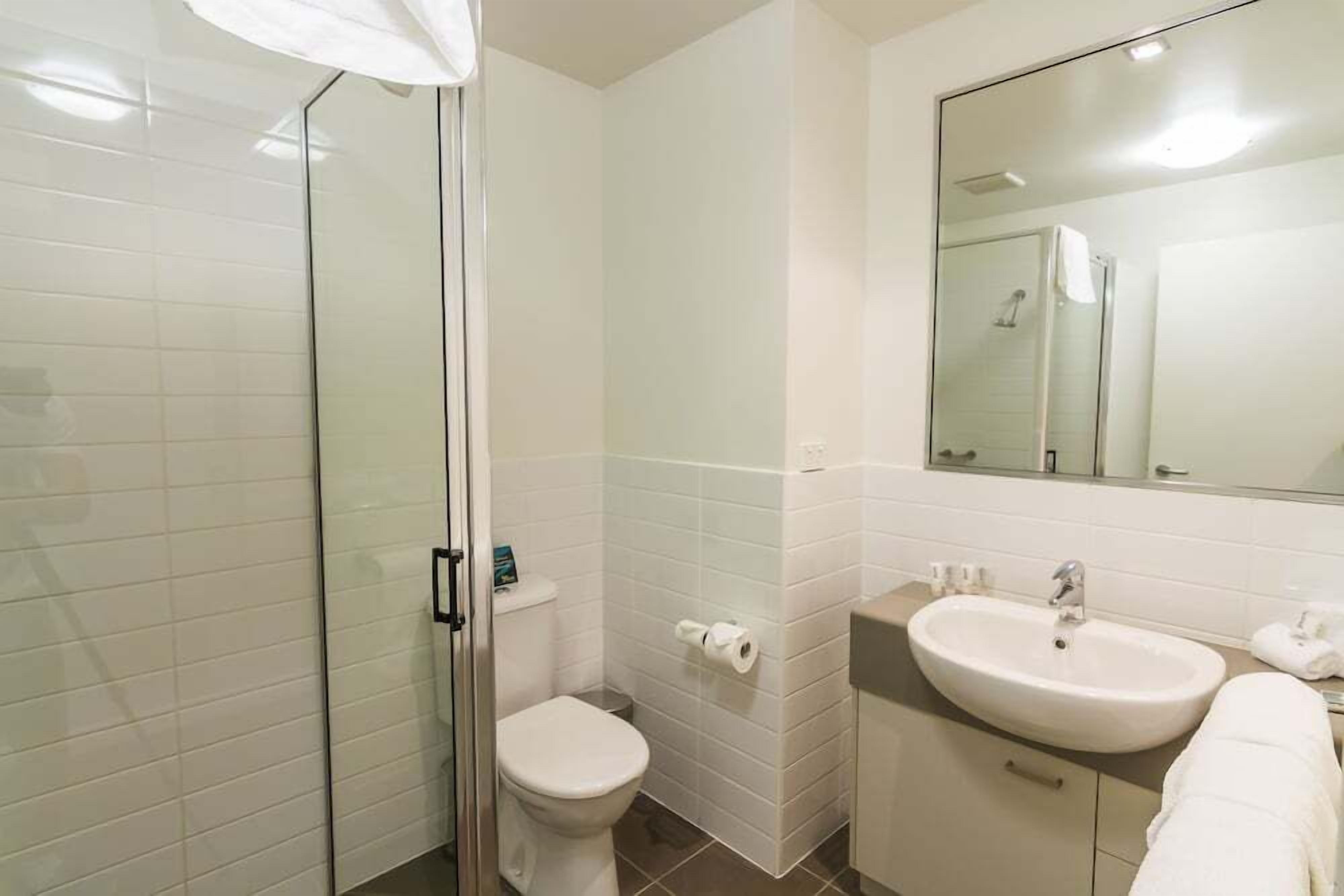 A bathroom with a glass shower enclosure, a toilet, a sink, and a mirror.