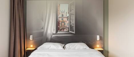 Habitación de hotel con cama, dos lámparas de noche, ventana con cortinas y vista a un edificio con torre de reloj.