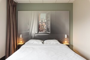 Habitación de hotel con cama, dos lámparas de noche, ventana con cortinas y vista a un edificio con torre de reloj.