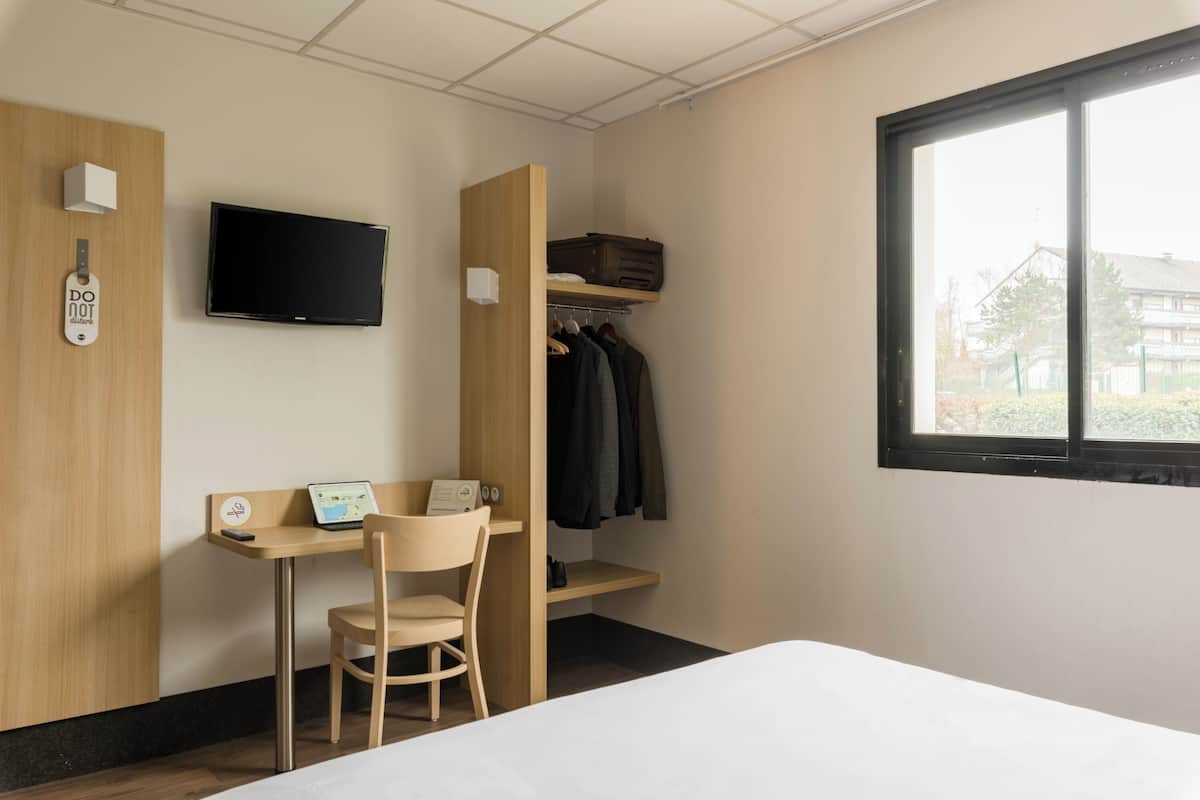 Una habitación de hotel con cama, escritorio con silla, televisor, armario y ventana.