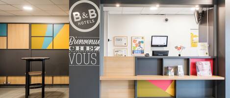 Una recepción con un cartel de B&B Hotels, un monitor de ordenador y varios carteles informativos.