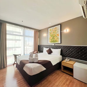 Ein Hotelzimmer mit einem großen Bett, einem Nachttisch mit Telefon, einem Sessel und einem Fenster mit Vorhängen.