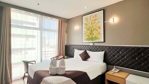 Ein modernes Hotelzimmer mit einem großen Bett, einem Schreibtisch, einem Stuhl und einem Fenster mit Vorhängen.