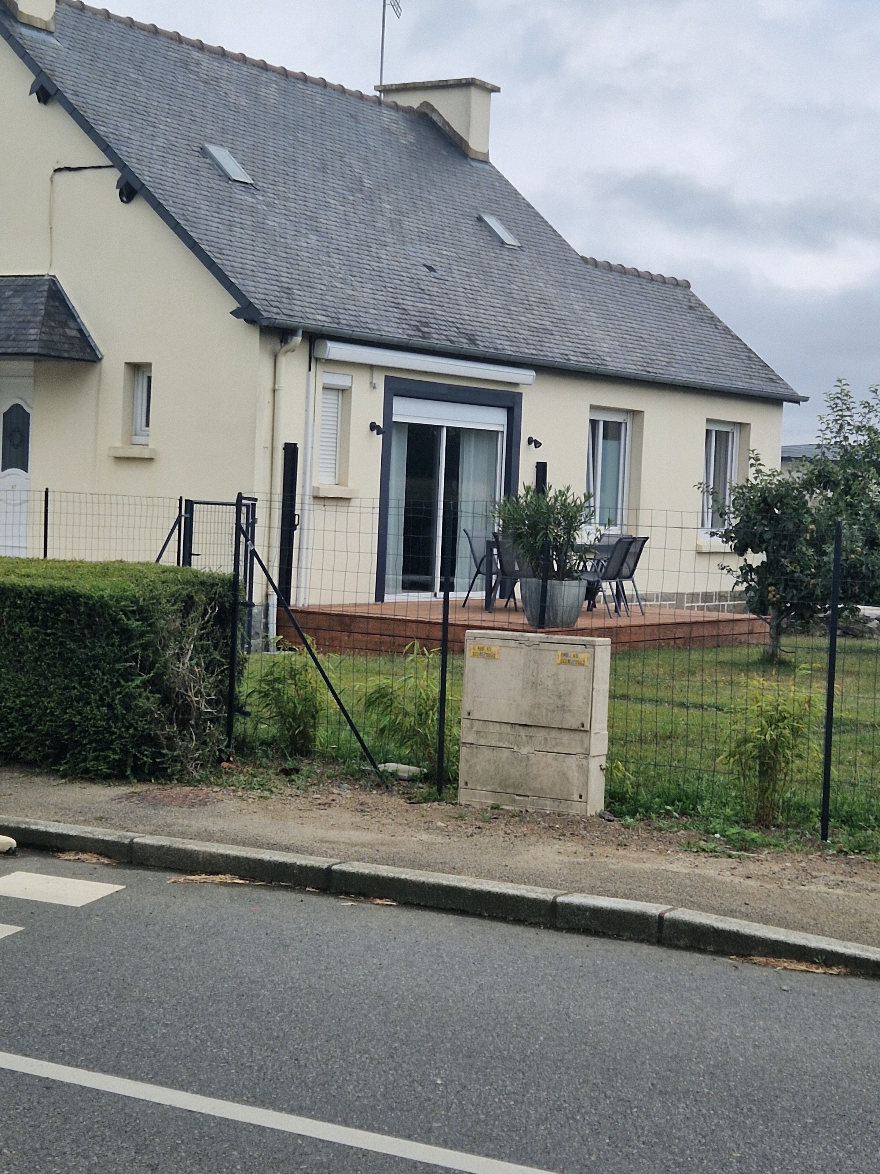 Une maison à deux étages avec un toit gris, une porte d’entrée dotée de panneaux de verre et un petit porche aménagé avec du mobilier d’extérieur.