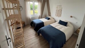 Een slaapkamer met twee bedden, een houten droogrek, een raam met gordijnen en een aan de muur hangende dreamcatcher.