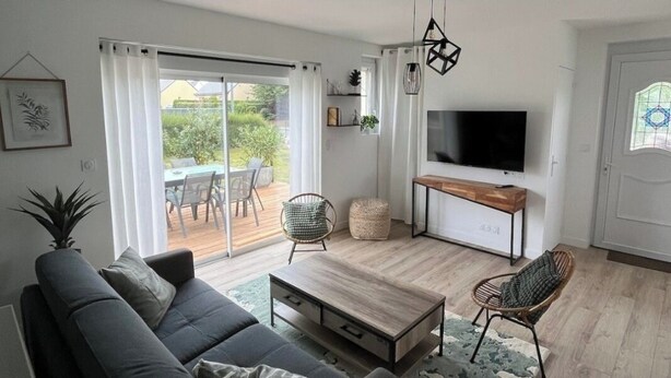 Een moderne woonkamer met een bank, salontafel en stoelen, een televisie en een schuifpui naar een terras.
