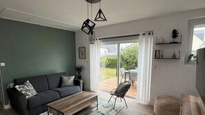 Een moderne woonkamer met een bank, salontafel en stoelen, een houten vloer en een uitzicht door een glazen deur op een buitengebied.