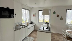 Een moderne keuken met witte kasten, een centraal eiland en een eethoek met een witte tafel en stoelen.