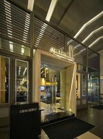 A modern hotel entrance with a concierge desk, glass doors, and a well-lit interior.
