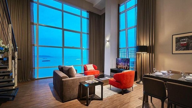 A spacious living room with large windows, a dining area, and a staircase.