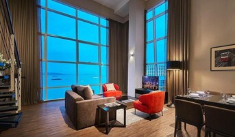 A spacious living room with large windows, a dining area, and a staircase.