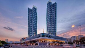 A modern hotel with a prominent glass facade, a covered entrance, and two tall buildings in the background.