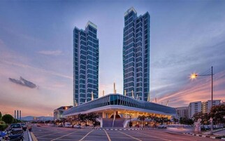A modern hotel with a prominent glass facade, a covered entrance, and two tall buildings in the background.
