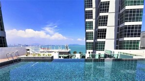 A rooftop infinity pool with a clear view of the sea and distant cityscape.