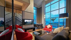 A modern living room with a large TV, red and brown sofas, a glass coffee table, and a view of the city through large windows.