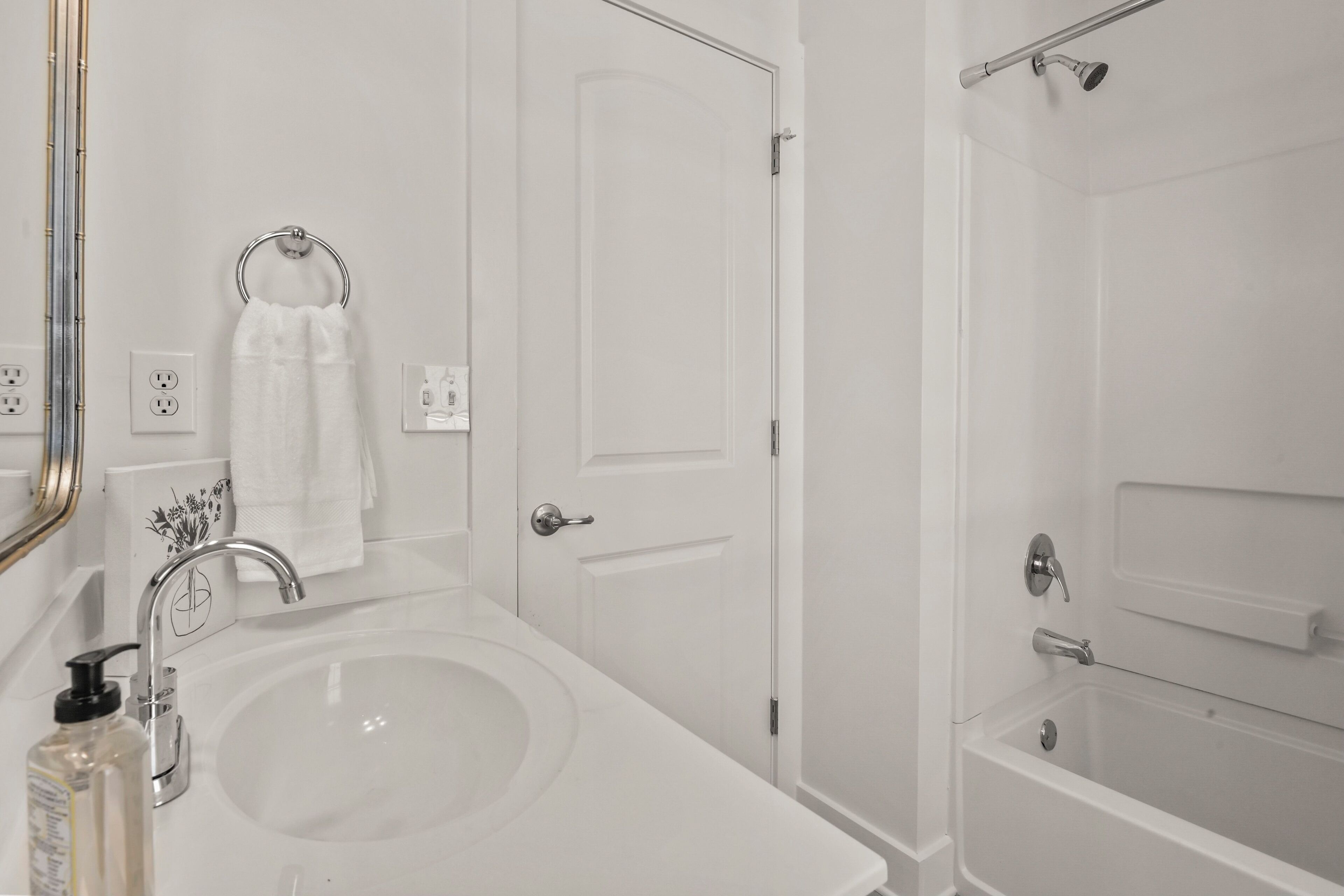 A bathroom with a white sink, a mirror, a towel ring, a door, and a shower area.