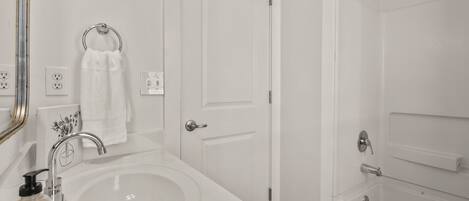 A bathroom with a white sink, a mirror, a towel ring, a door, and a shower area.