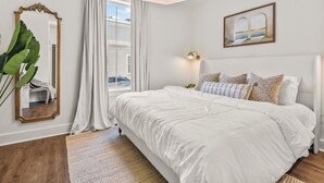 Ein Schlafzimmer mit einem großen Bett, einem Spiegel, einem Gemälde und einem Fenster mit Vorhängen.
