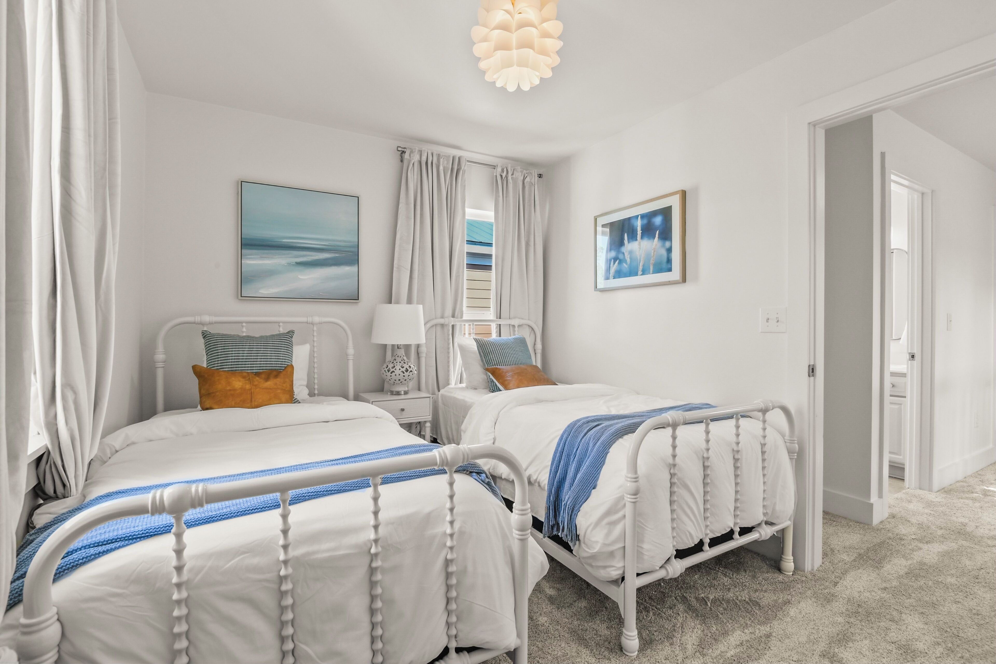 A bedroom with two beds, white bedding, and a view of the sea through the window.