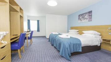 A hotel room with a bed, two bedside tables, a desk with a chair, a wardrobe, and a window with curtains.