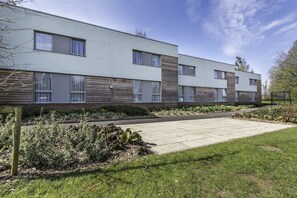 Un edificio moderno de varios pisos con techo plano, ventanas grandes y un camino pavimentado.